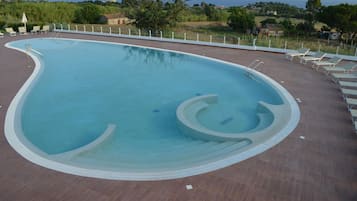 Une piscine au design incurvé, entourée d’une terrasse carrelée et de chaises longues.