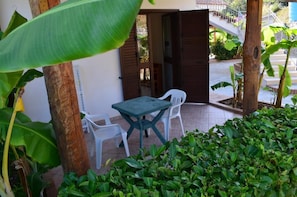 An outdoor seating area with a table and two chairs, surrounded by greenery and a wooden door. - Luzia Agriresort (Ricadi)
