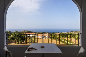 A balcony with a table and chairs, overlooking a coastal landscape with houses and greenery. - Luzia Agriresort (Ricadi)
