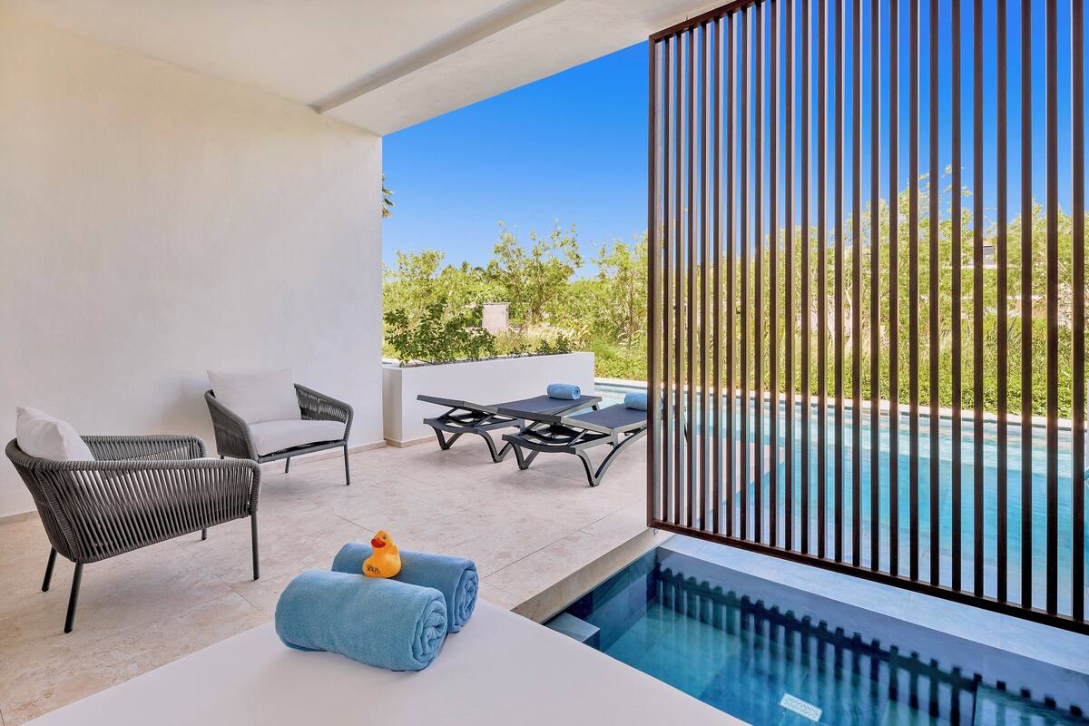 Ein Balkon mit Pool, Korbmöbeln und Blick ins Grüne.