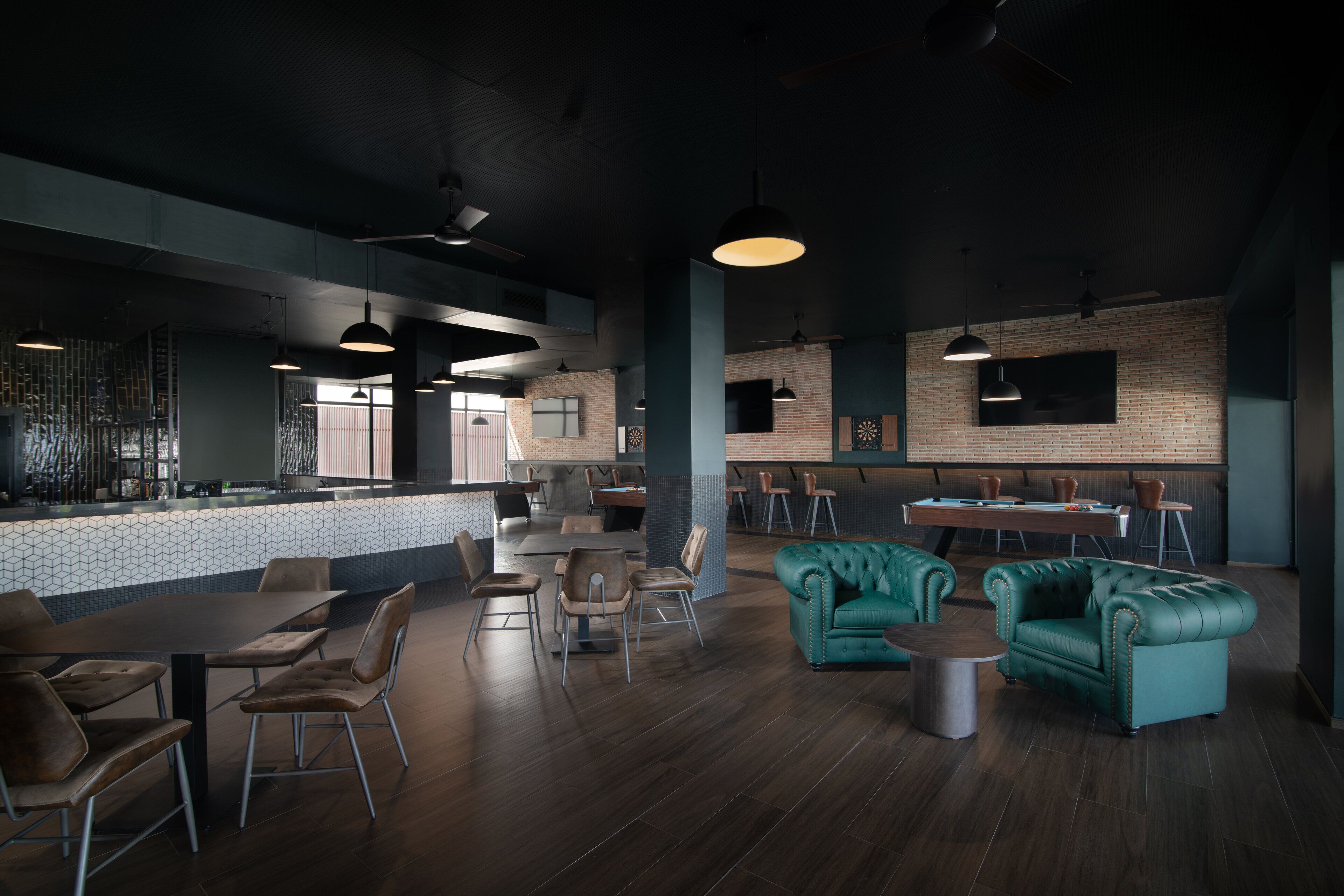 Un restaurante moderno con piso de madera oscura, sofás tapizados en color verde azulado e iluminación colgante.