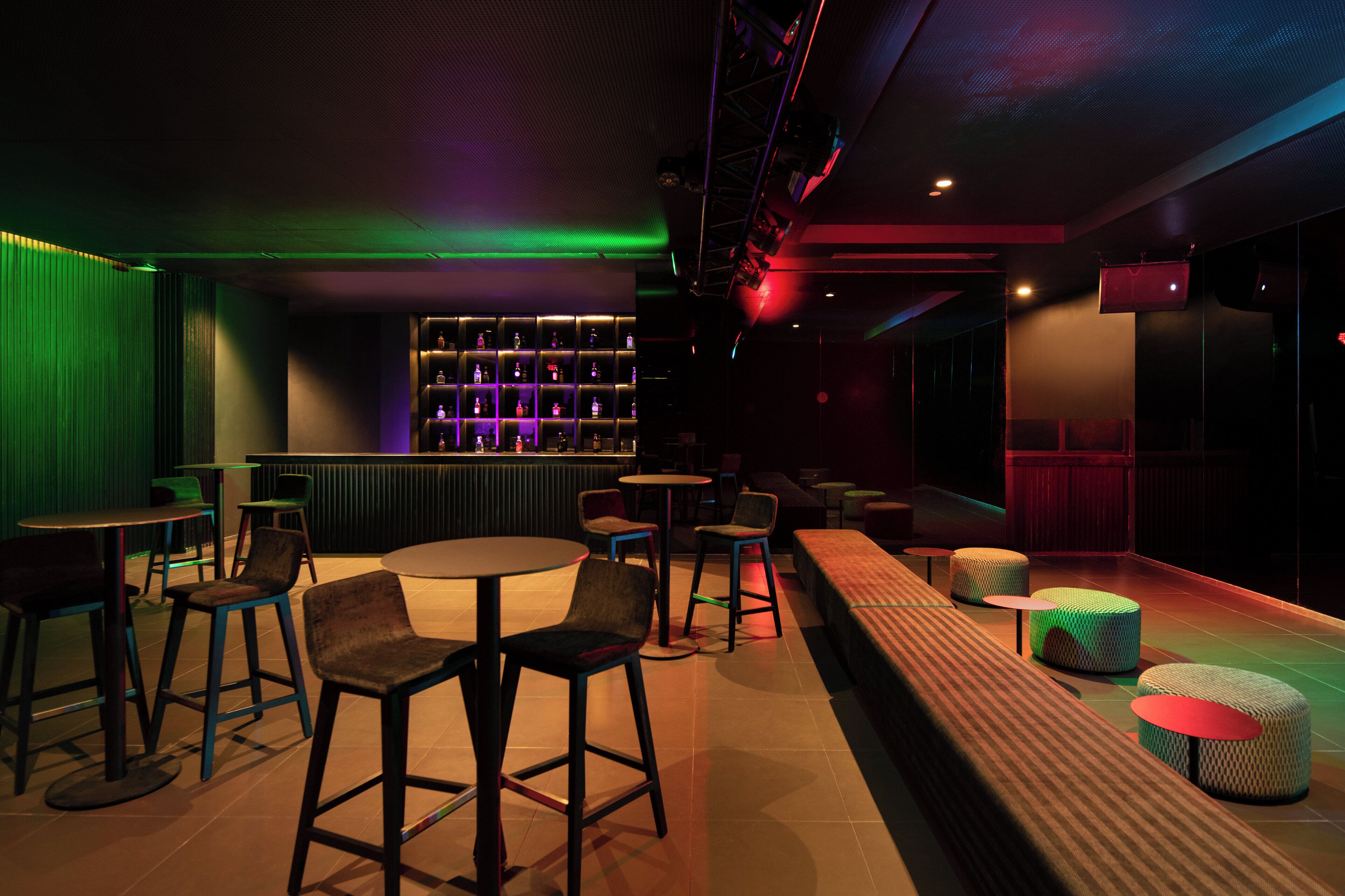 A bar area with stools, tables, and a bar counter with shelves of bottles.