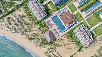 Luchtbeeld van een resort met diverse zwembaden, strandgebieden en weelderige beplanting.