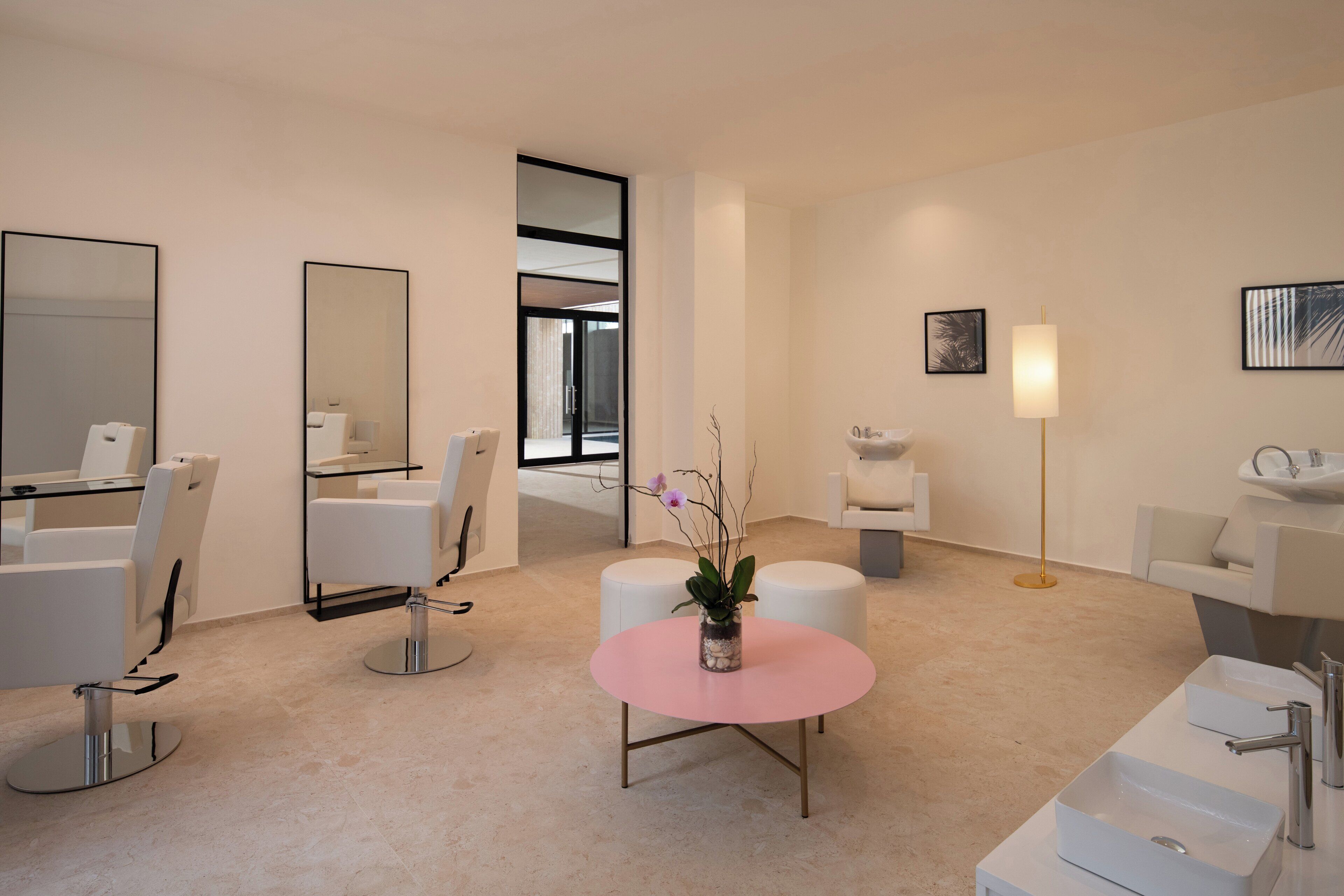 A modern hotel room with a large mirror, two white chairs, a pink table with a vase, and a large window.