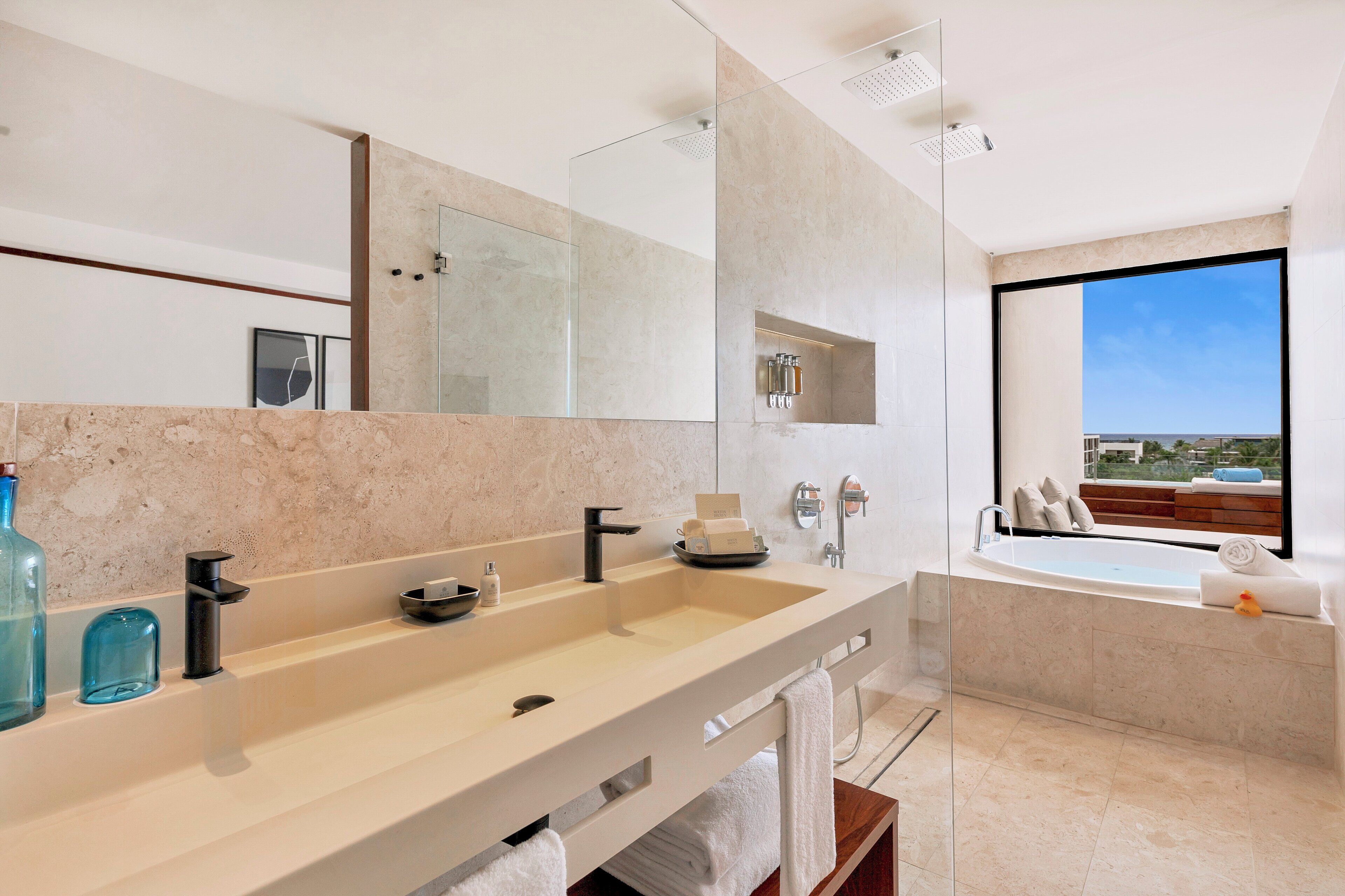 A modern bathroom with a large mirror, two sinks, a bathtub, and a view of the city.