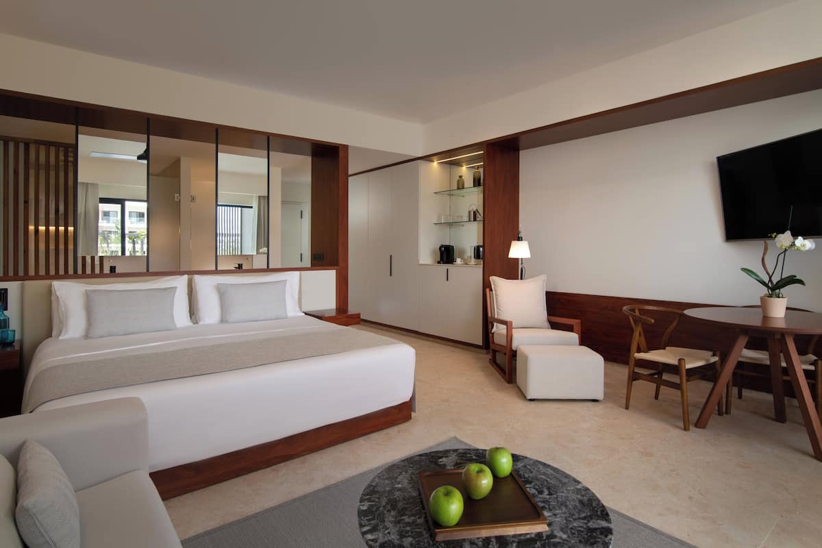 Ein modernes Hotelzimmer mit einem großen Bett, einem Schreibtisch, einem Stuhl und einem Esstisch. Ein Flachbildfernseher ist an der Wand befestigt und auf dem Tisch steht ein Blumentopf.