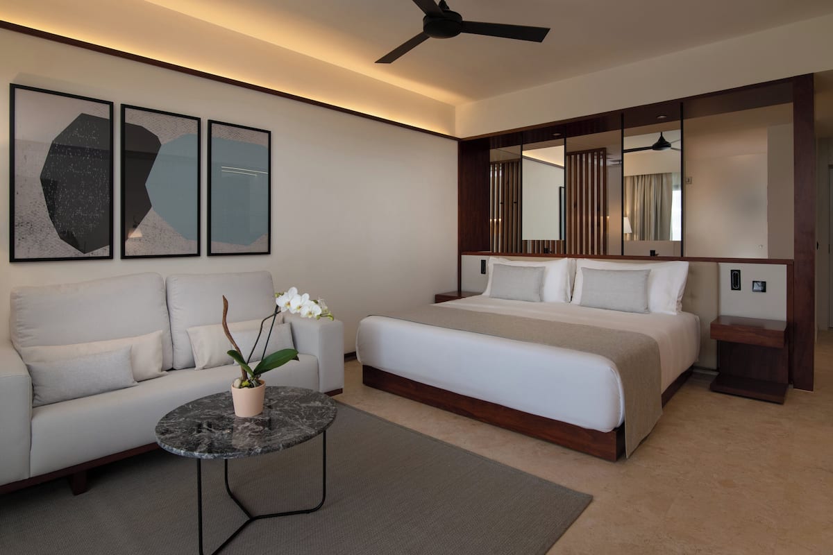 Ein modernes Hotelzimmer mit Bett, einer Couch, einem Couchtisch und einem Deckenventilator.