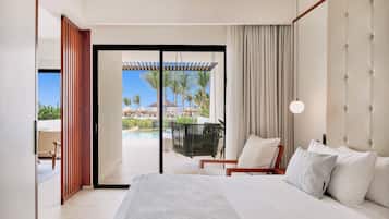 A modern hotel room with a large bed, a view of a pool and palm trees, and a sliding glass door leading to an outdoor area.