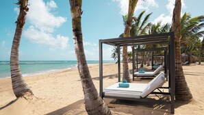 Een hotel aan het strand met een bed in de vorm van een hangmat, palmbomen en uitzicht op de oceaan.