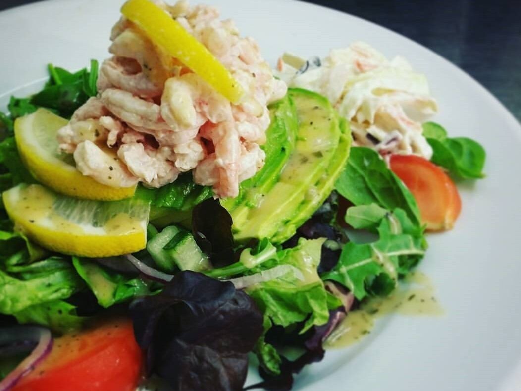 Een salade met diverse groenten en garnalen erover.