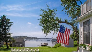 A waterfront property with a flag, a lawn with chairs, and boats in the background. - Dew Drop 2 Village Cottage, Steps to Harbor, Lawn & Boathouse (Port Clyde)