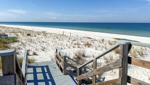 A wooden boardwalk leading to a sandy beach with clear blue water.
