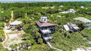 An aerial view of a coastal property with multiple buildings, including a central structure with a large balcony and a smaller building with a white facade.