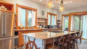 A spacious kitchen with a large island, wooden chairs, and a ship's wheel decoration.