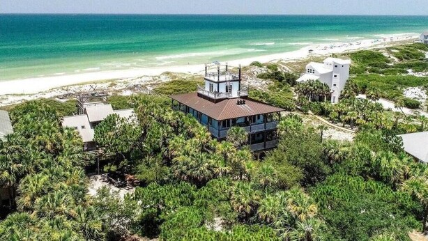 A beachfront property with a central building surrounded by dense vegetation, overlooking a sandy beach and the ocean.