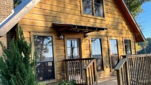 A wooden cabin with a porch, large windows, and a brick structure adjacent to it.