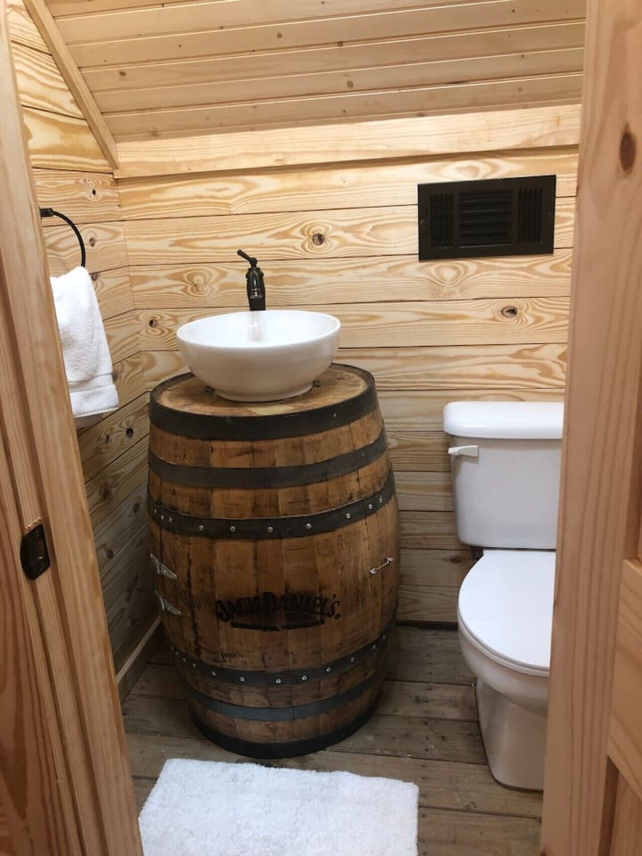 Une salle de bain rustique, aménagée dans une cabane en bois, avec un lavabo en forme de tonneau, des toilettes et un porte-serviettes.
