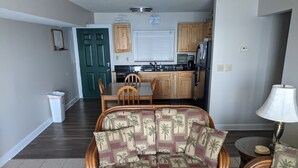 A living room with a sofa, a coffee table, and a lamp. There is a dining table with chairs and a kitchen in the background. - MBI Sunrise Waterfront Condo - Beautiful Lake Views (Middle Bass)