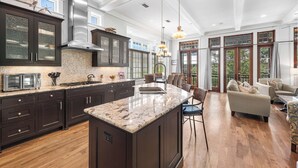 A spacious kitchen with dark cabinetry, a large island, and a dining area with a sofa and chairs. - Webb Isle Cottage - Close to Shopping, Dining & the Beach! Free Fitness/Tennis (Panama City Beach)
