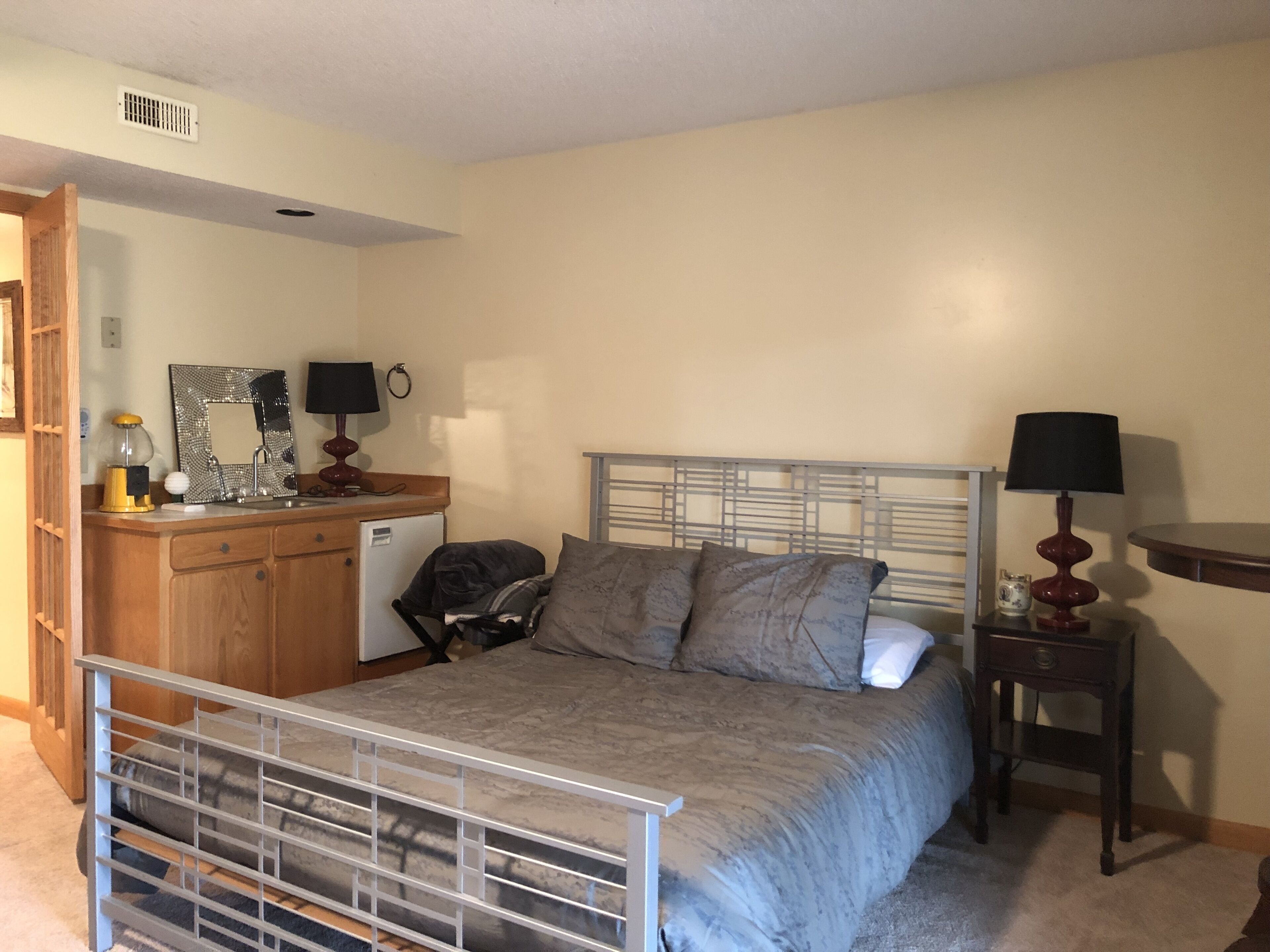 A bedroom with a bed, bedside table, dresser, and a small desk with a lamp.