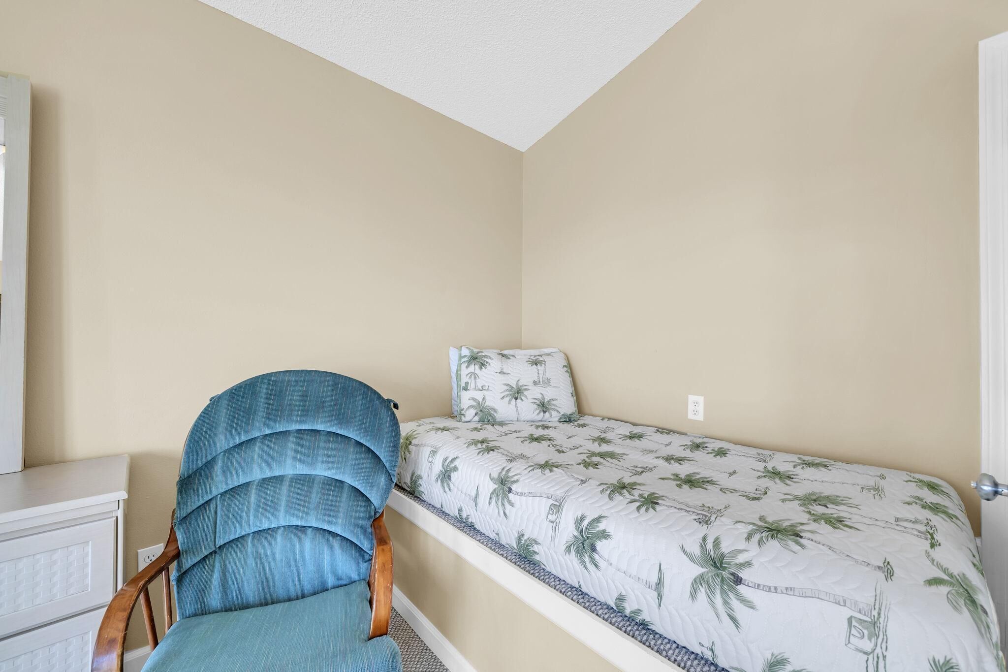 A small room with a bed, a chair, and a white dresser.