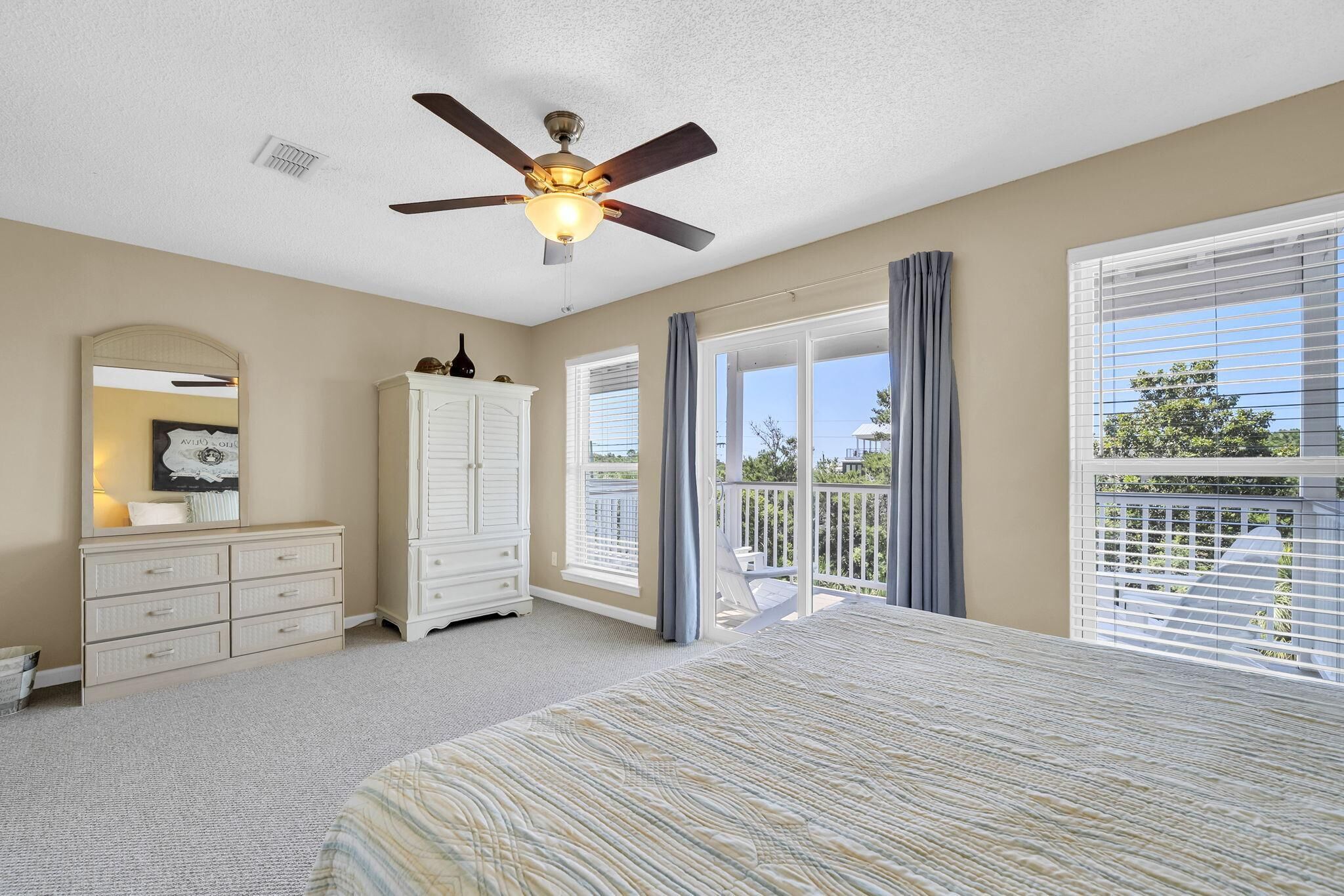 A bedroom with a bed, a ceiling fan, a dresser, a cabinet, and a balcony with a view.