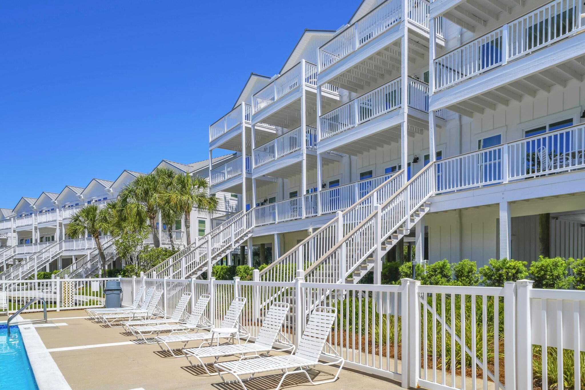 A multi-story hotel with balconies, a pool area with sun loungers, and a clear blue sky.