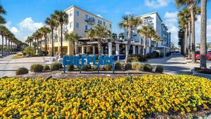 Un hotel con un patio central adornado con flores amarillas, rodeado de palmeras y un cielo azul despejado.