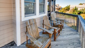 Eine Holzterrasse mit drei Adirondack-Stühlen und einem Geländer.