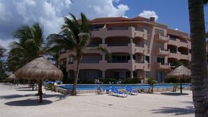 Un hôtel doté d’une piscine, de palmiers et de parasols en feuilles de palmier.