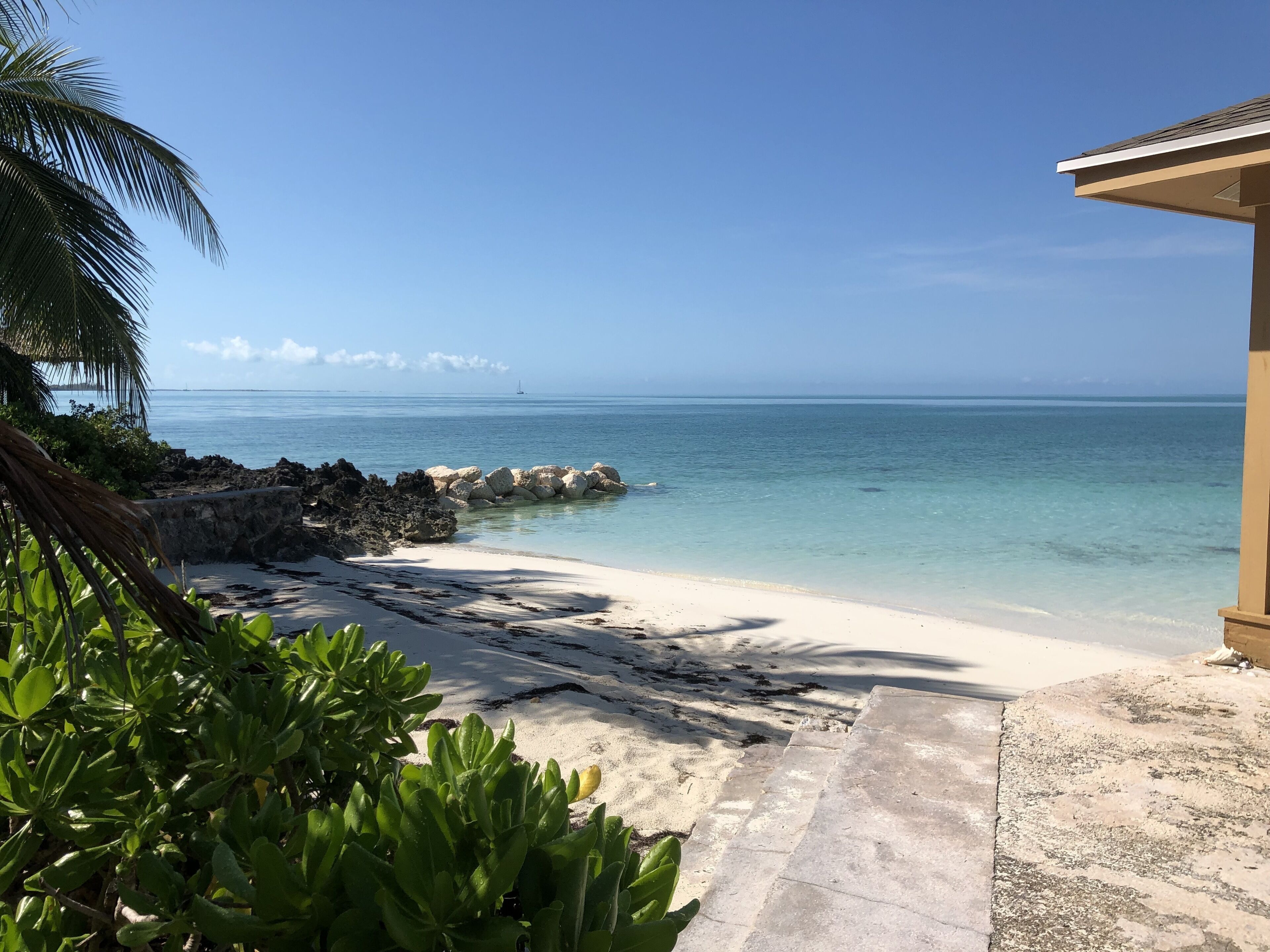A beach with clear turquoise water, a sandy shore, and a rocky outcrop.