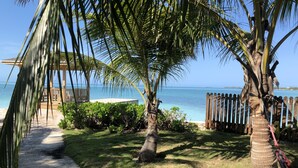 A pathway leading to a wooden deck overlooking a beach with palm trees and a fence.