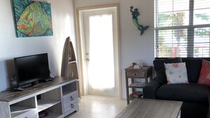 A living room with a TV on a wooden stand, a sofa with decorative pillows, a coffee table, and a colorful rug.