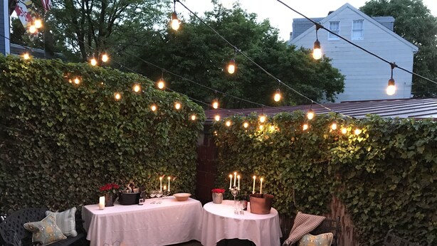 An outdoor patio with two tables set up, surrounded by ivy-covered walls and string lights.