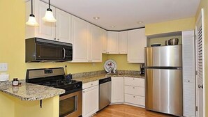 A compact kitchen with white cabinets, a stainless steel refrigerator, a microwave, and a stove.