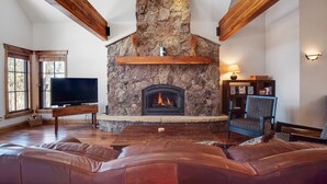 Ein Wohnzimmer mit Kamin aus Stein, Ledersitzmöbeln, Holzbalken und einem Fernseher.