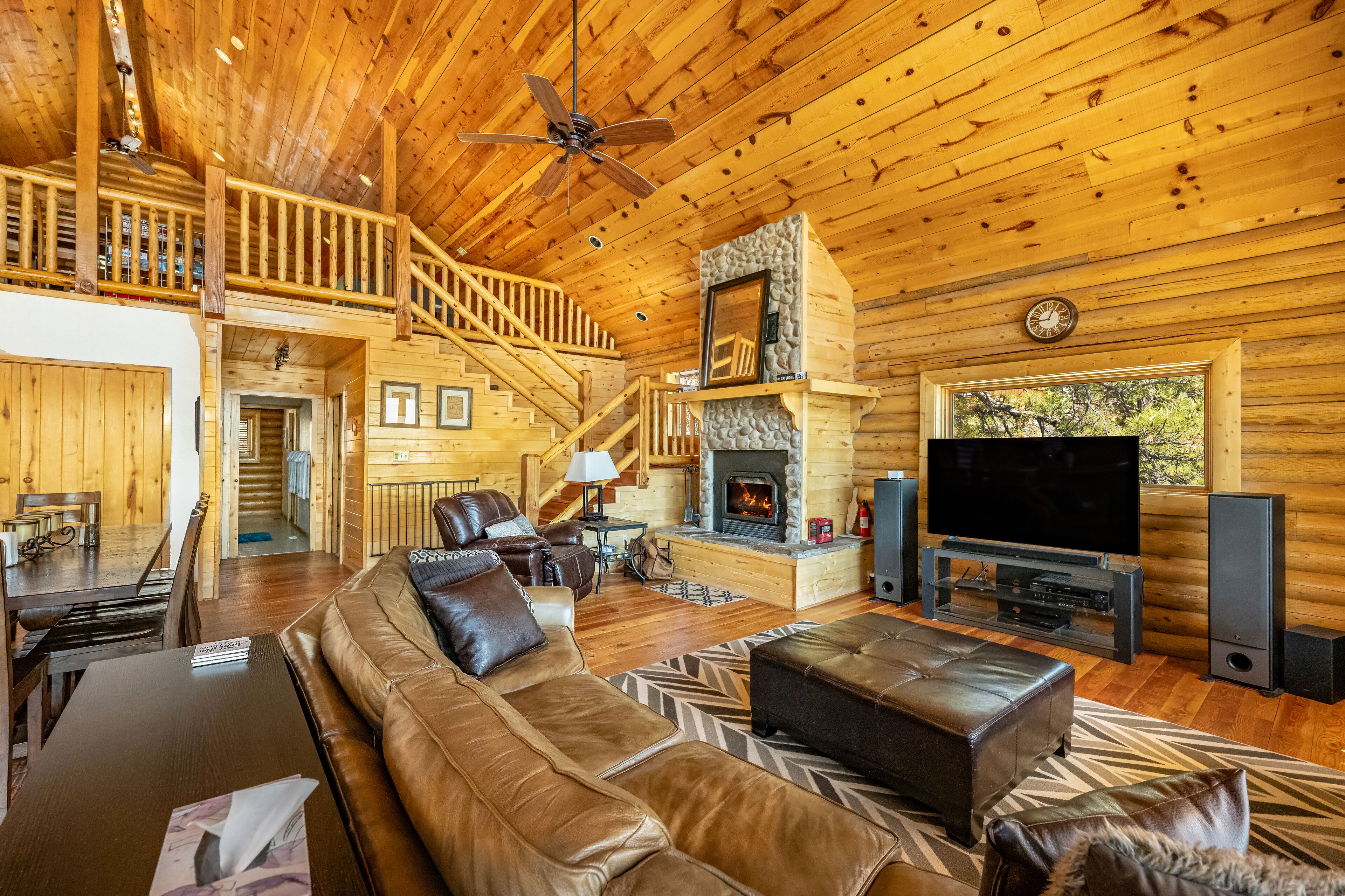 A log cabin interior with a living room, fireplace, TV, and a staircase leading to a loft.