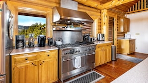A modern kitchen with wooden cabinetry, stainless steel appliances, and a large window offering a view of the outdoors.