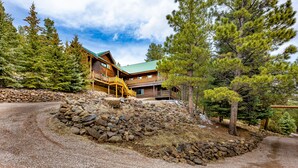 A lodge with a stone retaining wall, wooden deck, and a green roof.