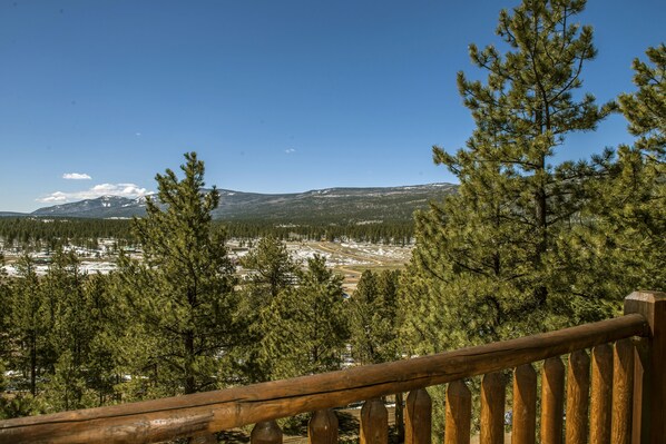 Una terraza de madera con vistas a un paisaje nevado, con pinos y montañas a lo lejos.