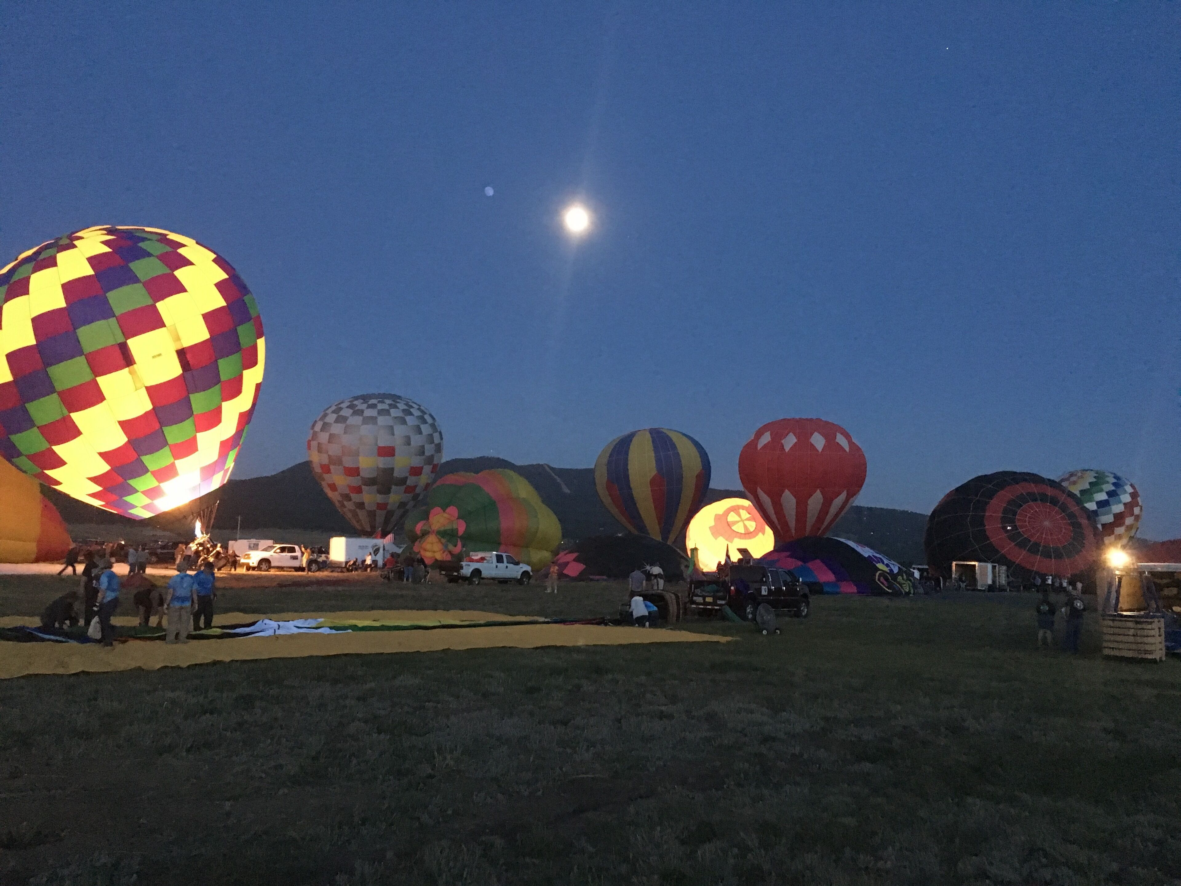 A field with multiple hot air balloons, some with people around them, and a clear night sky.
