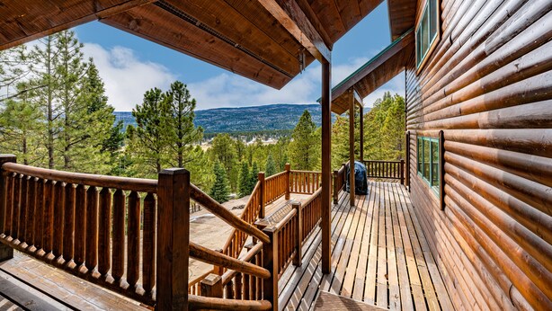 A wooden deck with a railing, overlooking a forested area and distant mountains.
