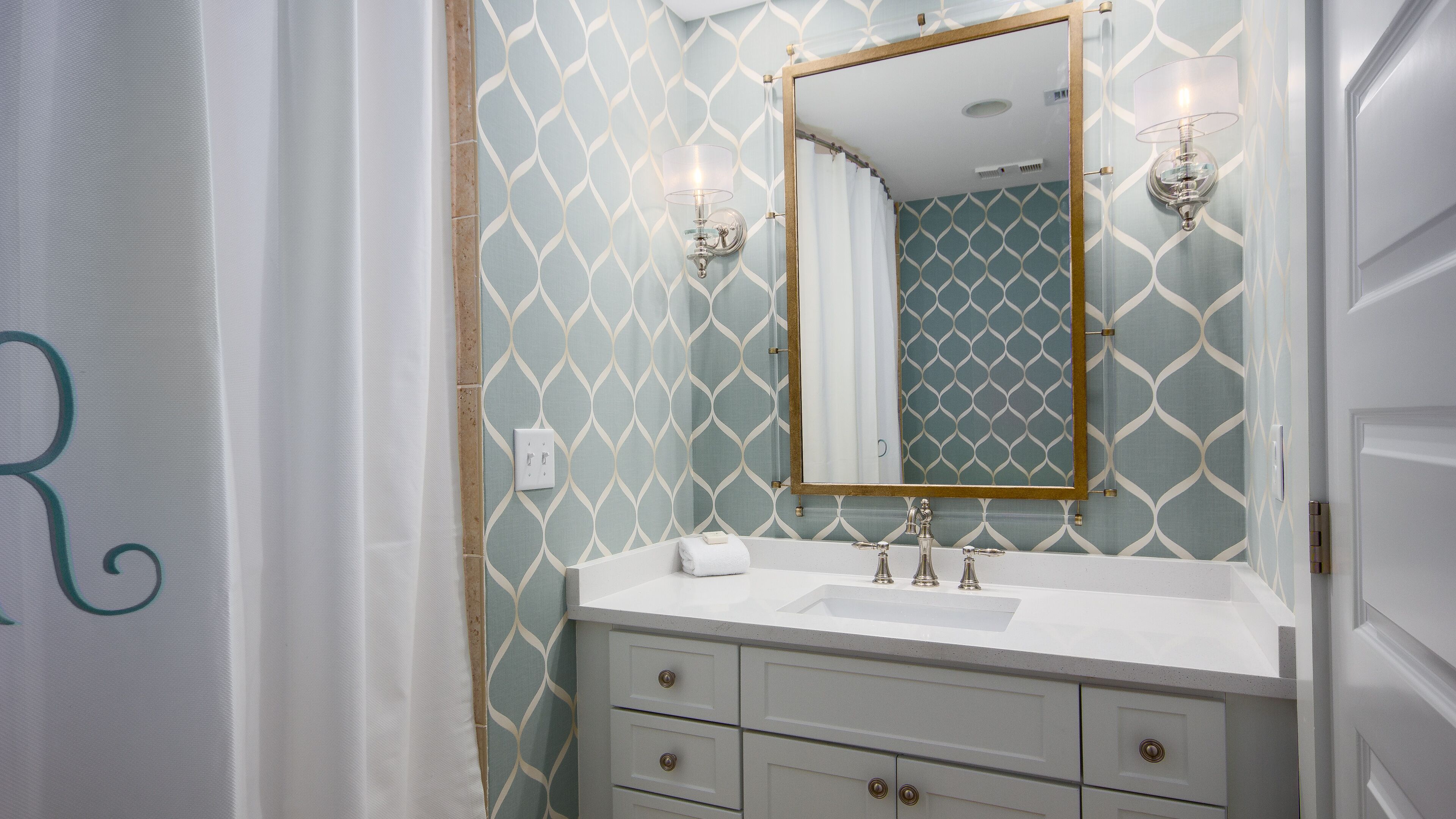Un bagno con un mobile lavabo bianco, uno specchio con cornice dorata e carta da parati decorata.