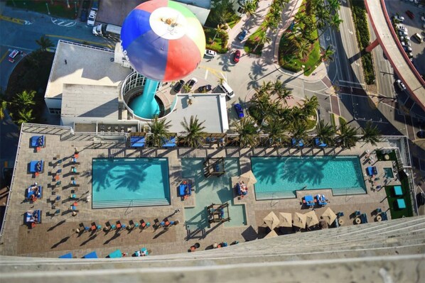Vista aérea de un hotel con dos piscinas, un área de juegos para niños y un amplio paraguas de playa.