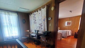 A room with a wooden floor, a sewing machine, a bed, and a window with curtains. - The Farm House at Peaks of Otter Winery and Orchards (Bedford)
