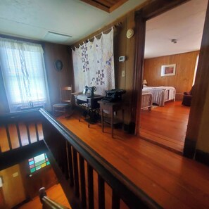 A room with a wooden floor, a sewing machine, a bed, and a window with curtains. - The Farm House at Peaks of Otter Winery and Orchards (Bedford)