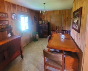 A wooden-paneled room with a dining table, chairs, a chandelier, and a door.