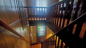 A wooden staircase with a handrail, a window with a stained glass design, and a door with a circular handle. - The Farm House at Peaks of Otter Winery and Orchards (Bedford)