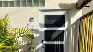 Una entrada moderna con una puerta blanca, escalones de piedra y un pequeño jardín con diversas plantas.