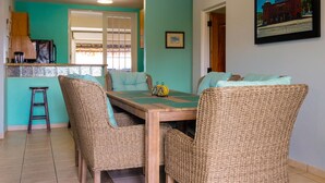 Un comedor con mesa de madera, sillas de mimbre y una cocina al fondo.